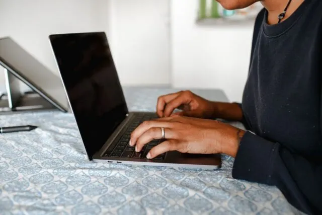 Birou ordonat cu laptop ridicat pe suport și o cană de ceai alături